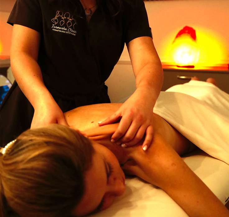 Osoba otrzymująca masaż pleców w gabinecie z relaksacyjnym oświetleniem.