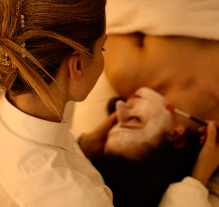 Kobieta nakłada maseczkę kosmetyczną na twarz klientki leżącej na łóżku zabiegowym w spa.